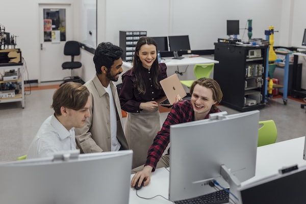 Four students gathering around a computer in a physics lab